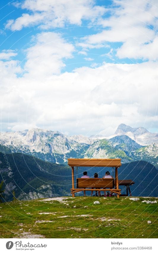 Touristen sitzen auf einer Bank oder Schaukelbank auf dem Gipfel des Berges Vogel in Slowenien und bestaunen das vor ihnen liegende Alpenpanorama . im Dreiländereck Slowenien - Österreich und Italien. Skigebiet Vogel, Slowenien