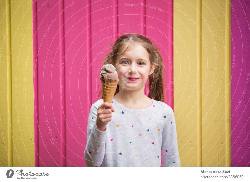 Süßes kleines Mädchen isst Schokoladeneis. Lächelnd und lachend. Bunte rosa und gelbe Wand im Hintergrund. Leuchtendes Sommerkonzept schön hell Café offen