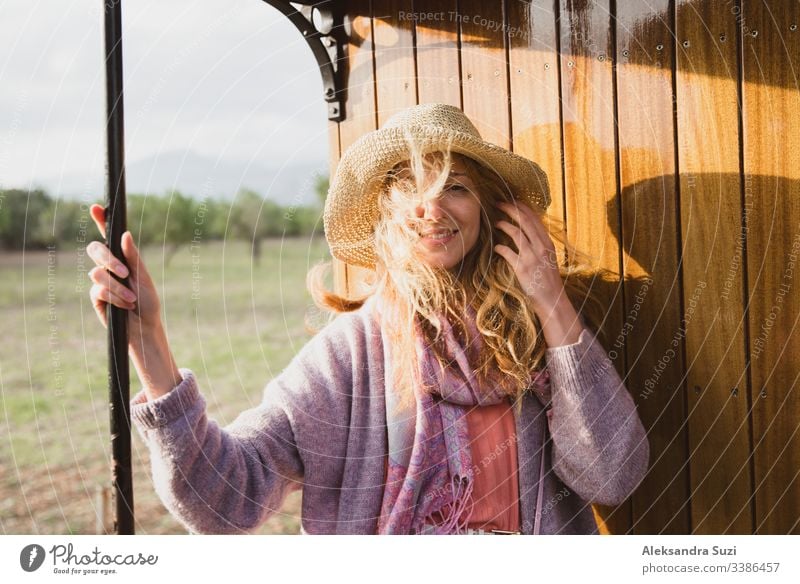 Junge Frau mit Strohhut reist mit einem Retro-Holzzug. Sonnenuntergangslandschaft, Wind in blonden Haaren. Mädchen lächelt fröhlich. Mallorca, Spanien.