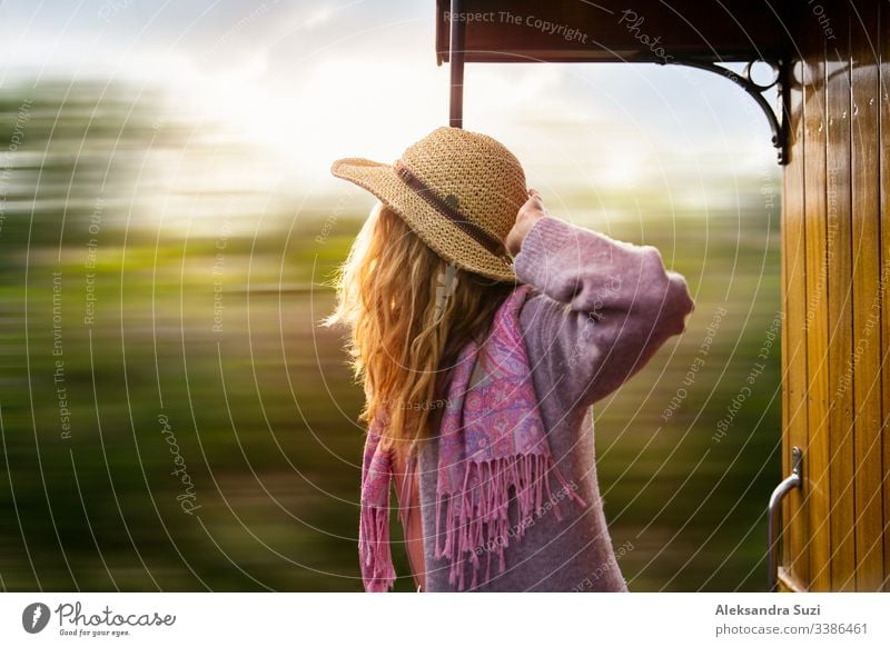 Junge Frau mit Strohhut reist mit einem Retro-Holzzug. Sonnenuntergangslandschaft, Wind in blonden Haaren. Mädchen lächelt fröhlich. Mallorca, Spanien.