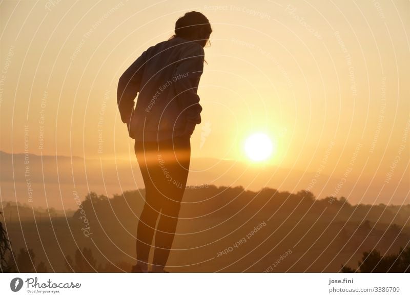 Frau steht vor Sonnenaufgang in der Toscana Natur Landschaft Bäume Berge Horizont Himmel Sonnenlicht orange hell Strahlen Außenaufnahme gelb Morgen wolkenlos