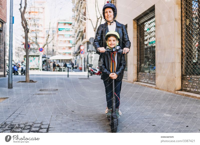 Mutter und Sohn auf einem Elektroroller mit Helm aktiv Junge lässig Kind Großstadt Tag E-Roller Öko elektrisch Europa Familie Frau Spaß Generation Schutzhelm