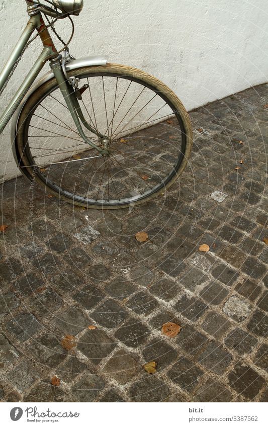 alt l altes, nostalgisches Rad im Retro-Stil, steht geparkt vor weisser, heller Hauswand auf Kopfsteinpflaster. Vorderteil, Lampe, Licht, Reifen von grauem Rad parkt in der Stadt.Diebstahlgefahr von altem Fahrrad, ungesichert, nicht abgeschlossen im Herbst