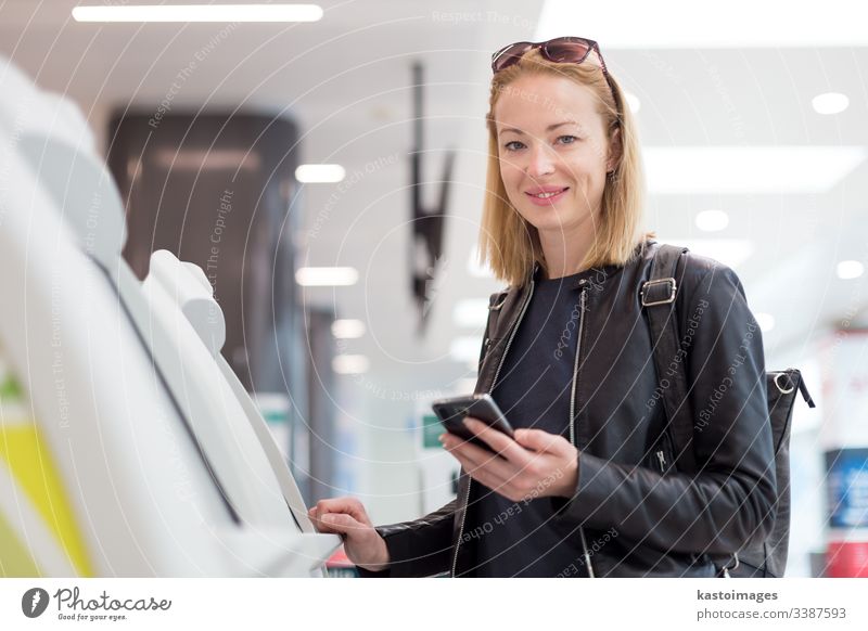 Lässige weiße Frau, die eine Smartphone-Anwendung und einen Check-in-Automaten am Flughafen benutzt, um die Bordkarte zu erhalten. Abheben Maschine Selbst