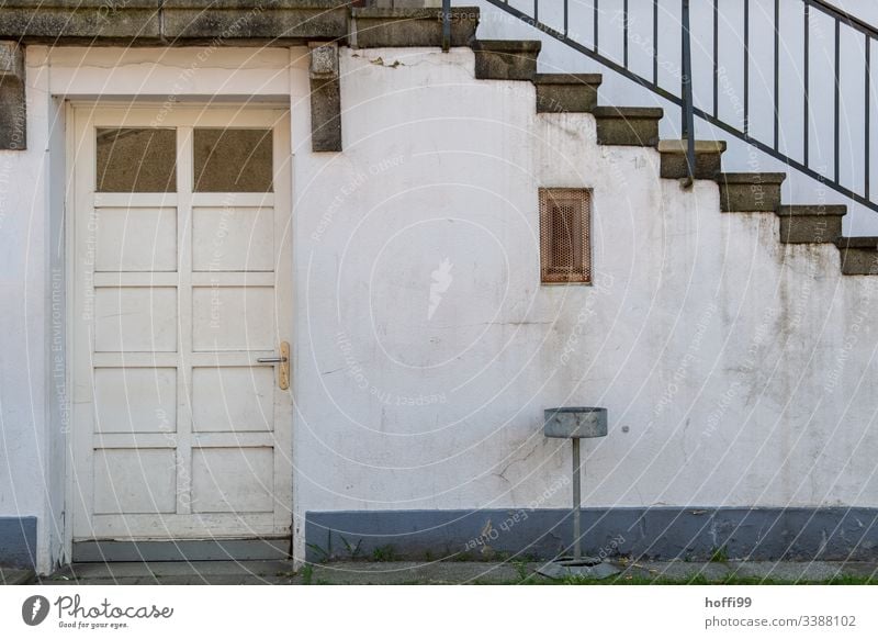 Treppe mit Geländer, Tür und  Aschenbecher vor dreckiger Wand diagonal Baustein minimalistisch Stufenordnung Treppenansatz Steinwand Ordnung Linien Muster