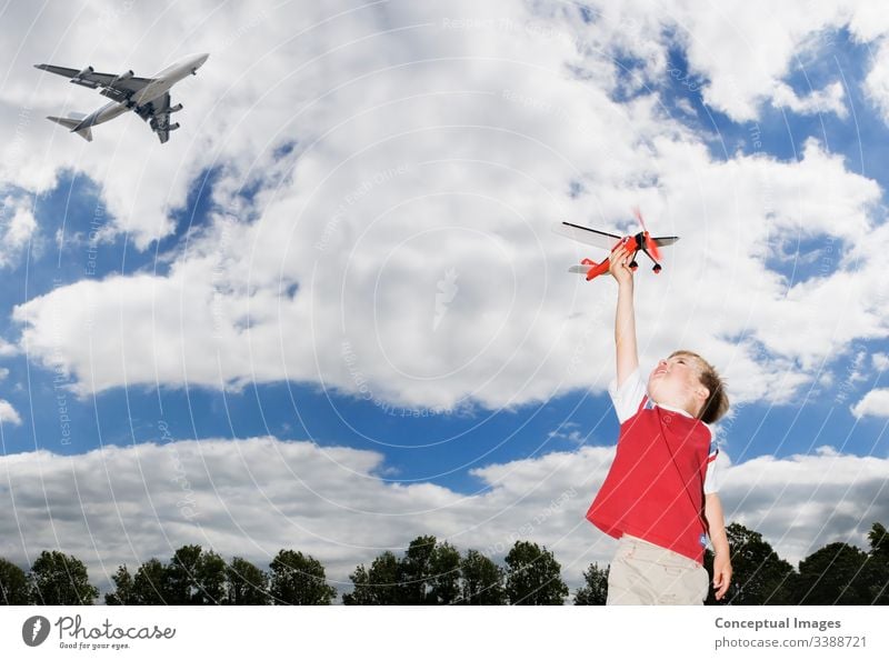 Junge Junge spielt mit einem SpielzeugflugzeugJunger kaukasischer Junge spielt mit einem Spielzeugflugzeug, während ein Passagierflugzeug über die Köpfe fliegtThemen der zukünftigen Phantasie Inspiration