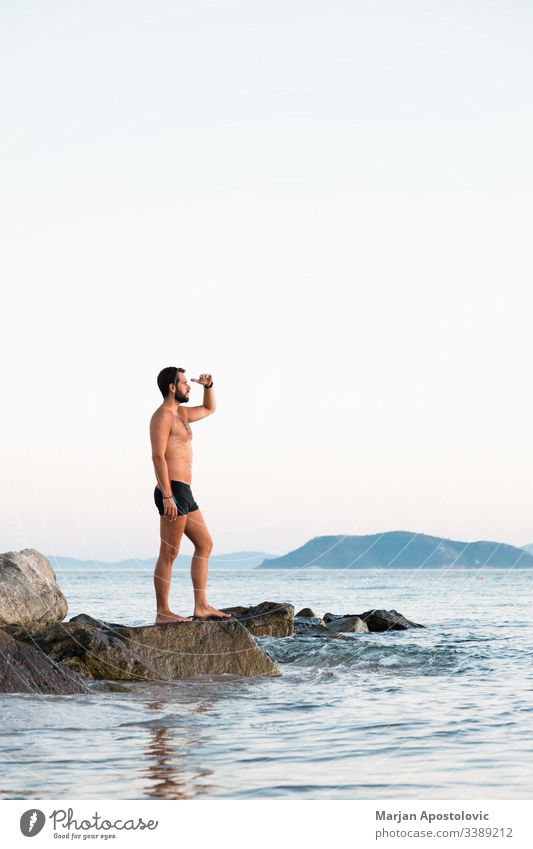 Junger Mann steht auf dem Felsen und genießt den Sonnenuntergang am Meer Erwachsener allein Hintergrund Strand Windstille Kaukasier Küste Abenddämmerung