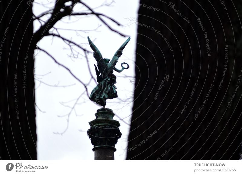 Auf einer von winterlich kahlen Bäumen umgebenen Siegessäule tanzt, so scheint es, ein Engel mit mächtigen Flügeln und weitem Kleid auf einem Bein und schwenkt einen Siegeskranz in der Hand eines angewinkelt ausgestreckten Arms