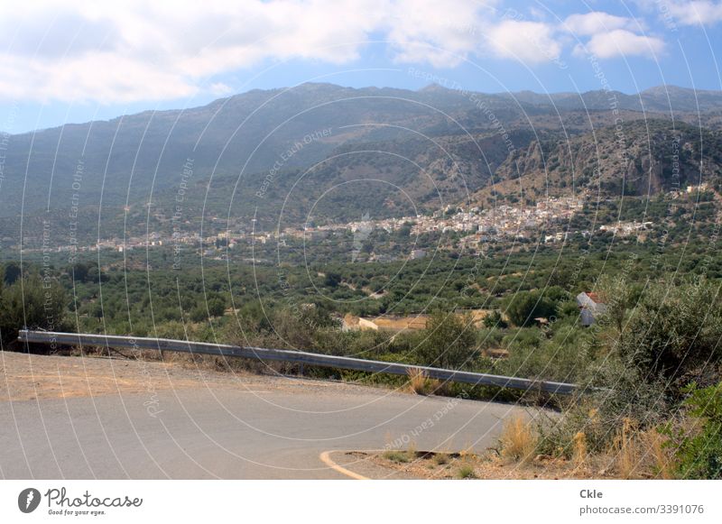 Kretische Bergstraße mit Ausblick auf Kritsa Kreta Griechenland Insel Bergdorf Straße Asphalt Leitplanke Abgrund Pflanzen Grün Bergwelt Dorf weiße Häuser Kirche