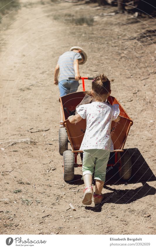 kleiner Junge und kleines Mädchen schieben einen Bollerwagen Urlaub Sommer Kinder Sonnenschein Familie Ausflug Geschwister Draußen entdecken erleben spazieren