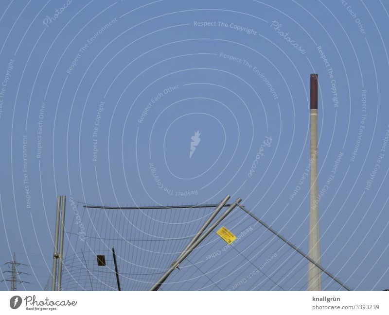 Bauzaun defekt vor Fabrikschornstein und Strommast Zaun Farbfoto Außenaufnahme Menschenleer Metall Barriere Licht Tag Gitter Sicherheit Muster kaputt Himmel