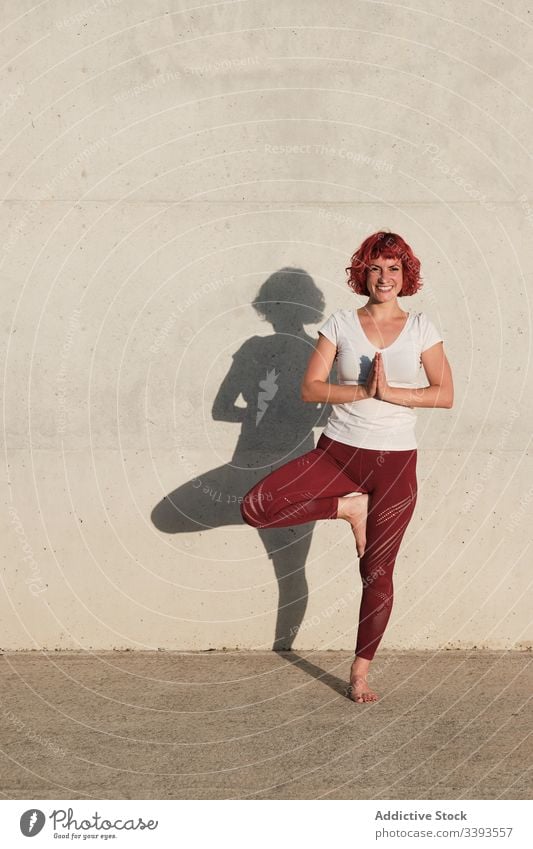 Frau macht Gleichgewichtsübung in Baumhaltung während sie Yoga auf der Straße praktiziert Athlet Namaste meditieren üben Training Übung Dehnung Barfuß Beton