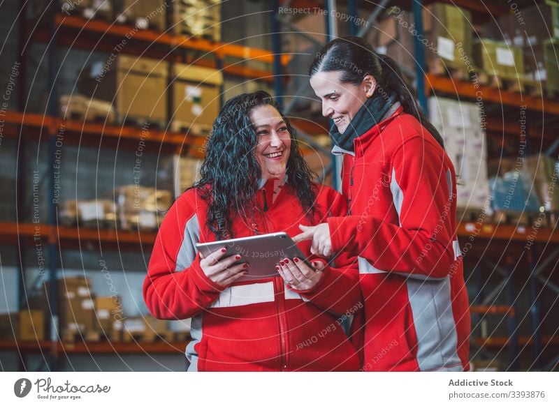 Zufriedene kluge Kolleginnen beim Surfen auf dem digitalen Tablet Lagerhalle Frauen Kollege benutzend Tablette Browsen Suche zuschauen Gerät Lächeln genießen