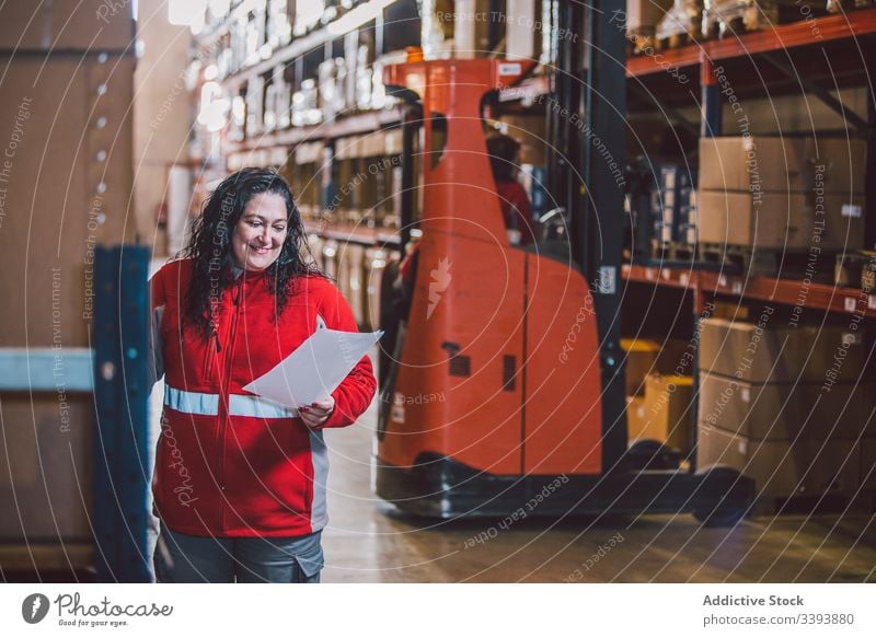 Zufriedene Dame in großem modernen Lagerhaus Lagerhalle Paket Unternehmen Frau Job lesen Schriftstück Kasten Produkt Versand Dienst Lächeln Information