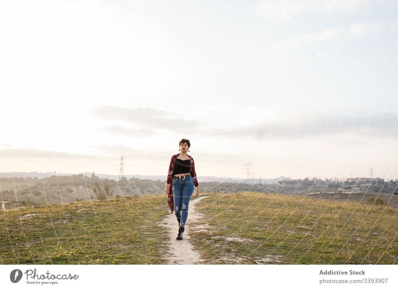 Hipsterin in trendigem Outfit auf leerer Landstraße Frau lässig Natur trendy Teenager Vorstadt Feld Landschaft Gras Himmel Lifestyle jung wolkig Spaziergang