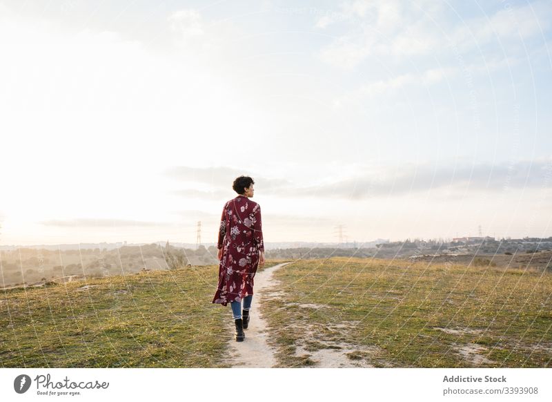 Anonyme weibliche Hipsterin in trendigem Outfit auf leerer Landstraße Frau lässig Natur trendy Teenager Vorstadt Feld Landschaft Gras Himmel Lifestyle jung