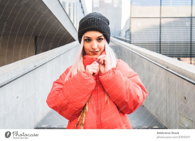 Zeitgenössische Frau in trendigem warmen Mantel auf der Straße Großstadt trendy warme Kleidung Hipster blond modern lässig Stil urban Treppe Hut Lifestyle