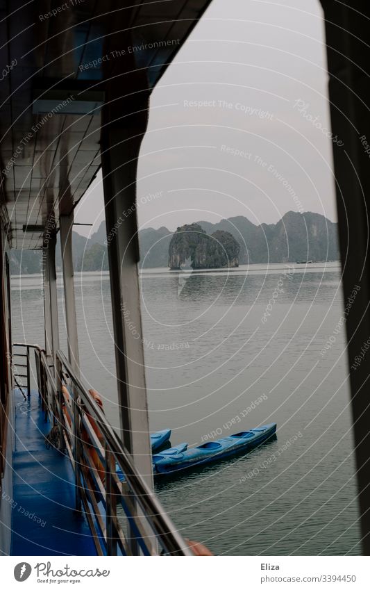 Aussicht von einem Ausflugsschiff, mit Reling und angebundenen Kajaks, in der Halong Bay in Vietnam; schöne Landschaft mit Kalksteinfelsen, die aus dem Meer ragen, bei nebligem Wetter