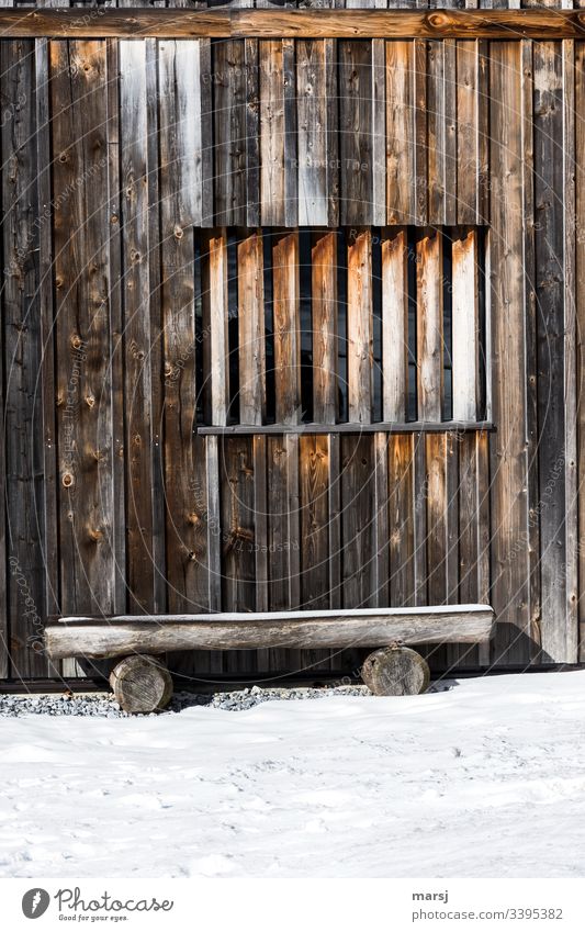 Schlichte hölzerne Bank vor einer Holzwand, mit einem Fenster, das mit Kanthölzern verbarrikadiert ist. braun Holzmaserung Wand Rechteck rechteckig geometrisch