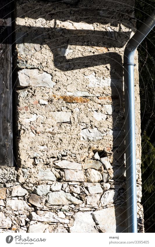 Schatten eines Regenrohrs auf einer Steinmauer Steinwand geschnallt gebeugt Fallrohr bügeln Steine Wand Haus Fassade Licht