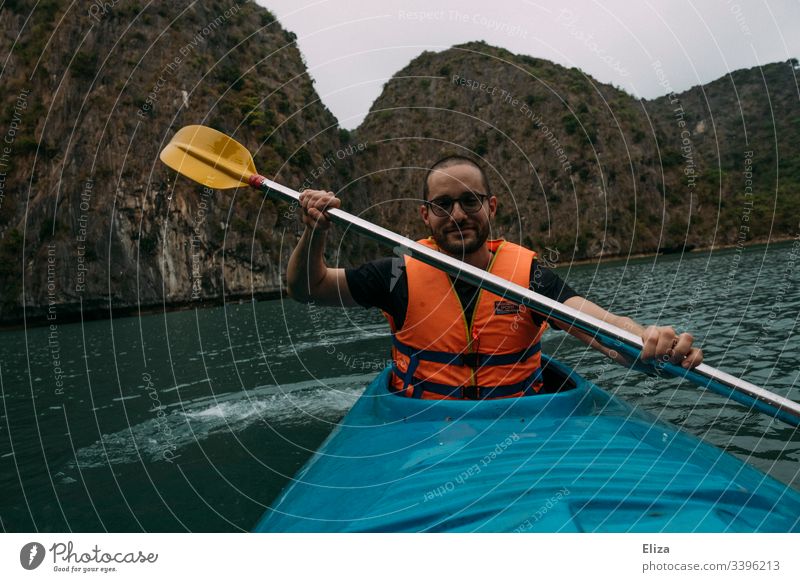 Mann mit Schwimmweste beim Kajaken in einem blauen Kajak in der Halong Bay in Vietnam Sport Natur Landschaft Tourismus Aktivurlaub Spaß sportlich Paddel