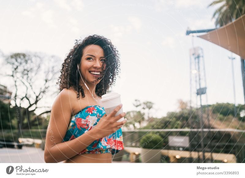 Afro-Frau, die Musik hört, während sie eine Tasse Kaffee hält. Kaffeetasse Kopfhörer Afro-Look Straße Ethnizität außerhalb stylisch zuhören Schönheit positiv