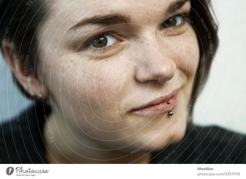 Portrait einer jungen Frau mit Lippenpiercing und Sommersprossen Blick nach vorn Porträt Zentralperspektive Schwache Tiefenschärfe Tag Nahaufnahme Innenaufnahme