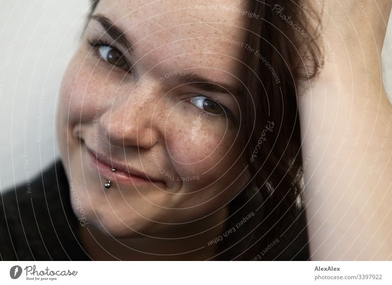 Portrait einer jungen Frau mit Lippenpiercing und Sommersprossen Blick nach vorn Porträt Zentralperspektive Schwache Tiefenschärfe Tag Nahaufnahme Innenaufnahme