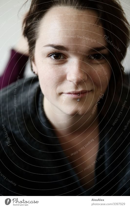 Portrait einer jungen Frau mit Lippenpiercing und Sommersprossen Blick nach vorn Porträt Zentralperspektive Schwache Tiefenschärfe Tag Nahaufnahme Innenaufnahme