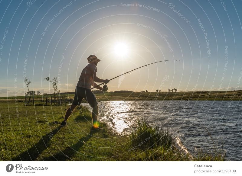 Junger Mann angelt am See, die Sonne steht tief, der Wind hat sich gelegt, die Fische sollten anbeißen Natur Umwelt Flora Pflanze Wiese Gras Wasser Gewässer