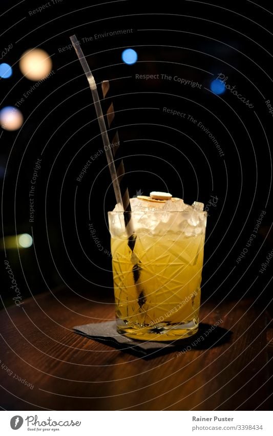 Köstlicher Cocktail mit zerstoßenem Eis in einer Cocktailbar mit Bokeh-Licht im Hintergrund Bar lecker geschmackvoll Nachtleben dunkel schwarz orange hölzern