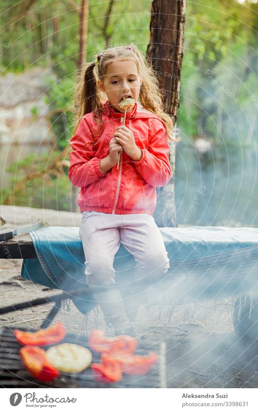 Mann und seine kleine Tochter grillen im Wald am felsigen Seeufer, machen ein Feuer, grillen Brot, Gemüse und Marshmallow. Familie erkundet Finnland. Skandinavische Sommerlandschaft.