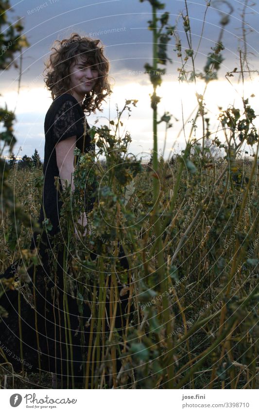 Junge Frau steht im hohen Feld, bei heller Sonne die durch dunkle Wolken bricht schön feminin Tag Außenaufnahme Natur natürlich frei Licht Sonnenlicht Locken