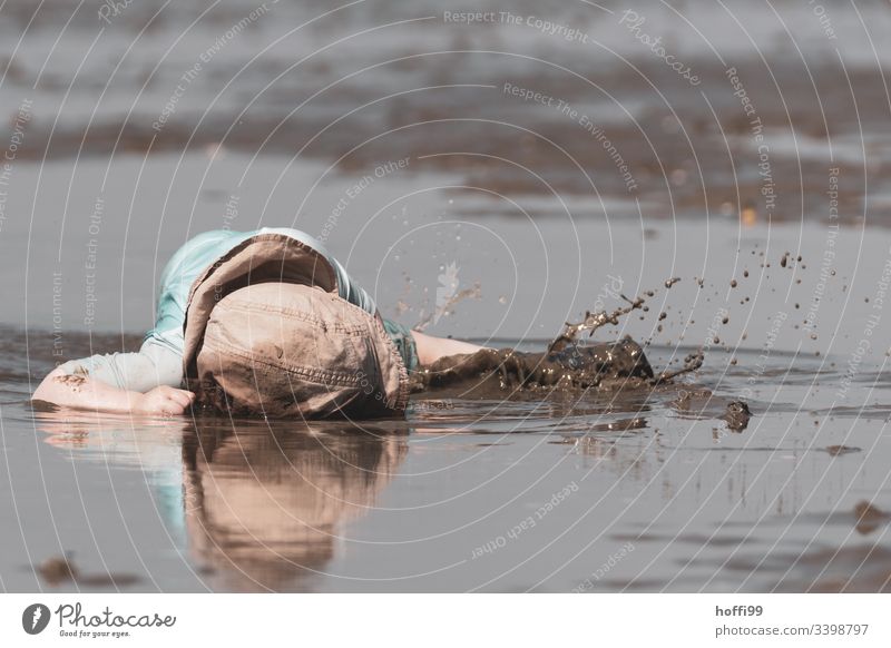 kleines Kind liegt im Matsch und langweilt sich Kleinkind Langeweile langweilig Ebbe Watt matschig spritzen nass Wasser Kindheit 1-3 Jahre Spielen Pfütze