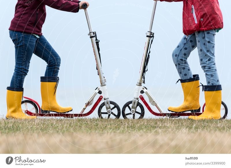 Roller Rad an Rad mit gelben Gummistiefeln Tretroller Spielen Kinder Spielzeug Spielplatz Duell