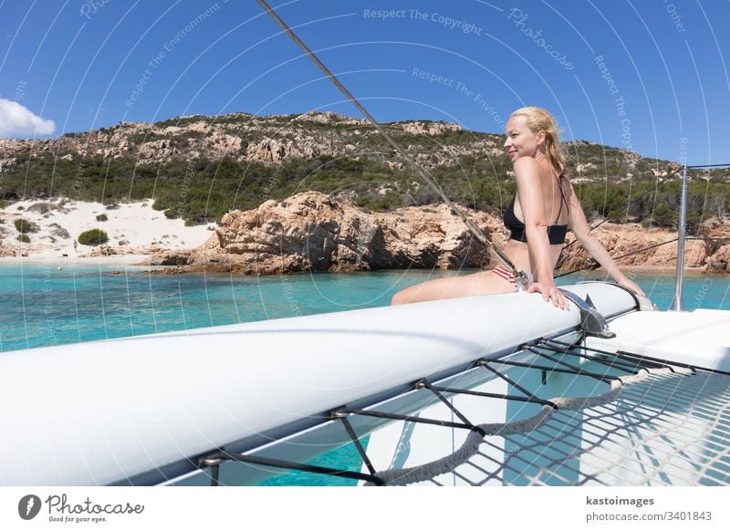 Frau entspannt sich auf einem Sommer-Segeltörn auf einem Luxus-Katamaran in der Nähe des bildschönen weißen Sandstrandes auf der Insel Spargi im Maddalena-Archipel, Sardinien, Italien.