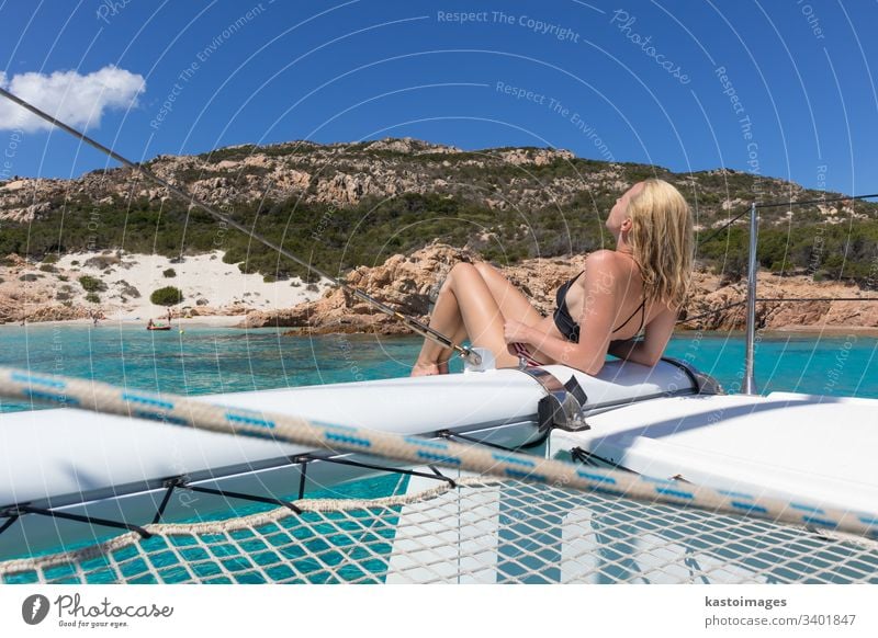 Frau entspannt sich auf einem Sommer-Segeltörn auf einem Luxus-Katamaran in der Nähe des bildschönen weißen Sandstrandes auf der Insel Spargi im Maddalena-Archipel, Sardinien, Italien.