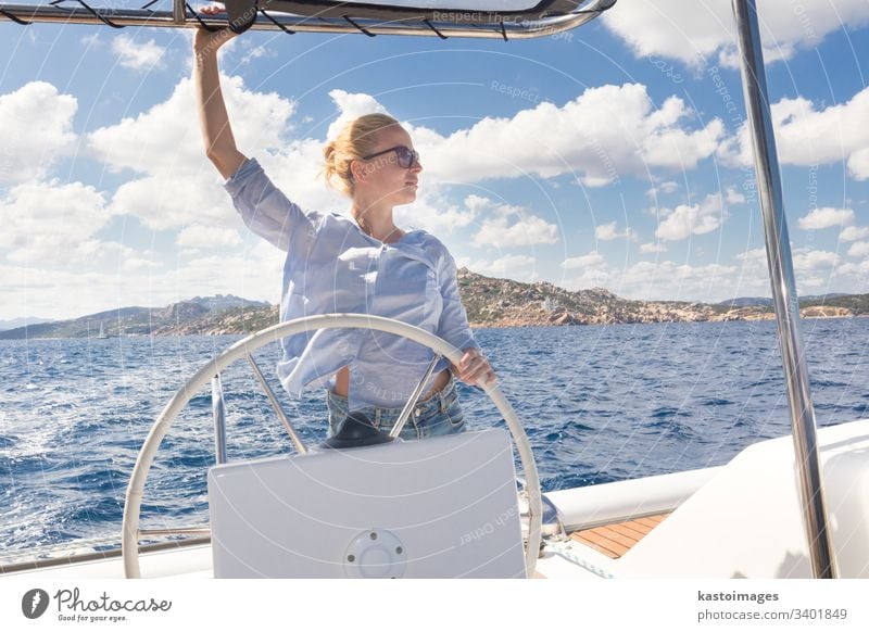 Attraktive blonde Skipperin, die das schicke Katamaran-Segelboot an einem sonnigen Sommertag auf ruhigem blauen Meerwasser steuert. nautisch Lenkrad Boot Frau