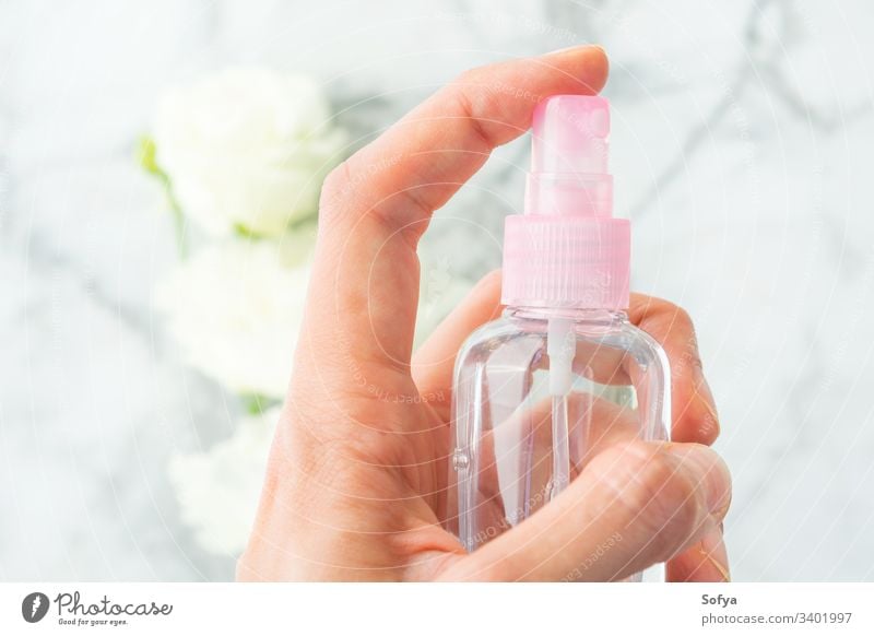 Frauenhand sprüht Flüssigkeit aus Spray über Marmorgrund mit weißen Blumen Flasche liquide Hand spritzend klein rosa Behaarung Produkt Hintergrund Schönheit