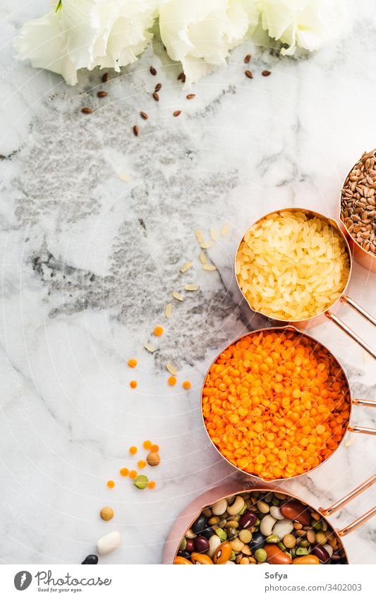 Kupferbecher mit Bohnen und Getreide und weißen Blumen auf Marmortisch Messung Tasse keine Verschwendung Lebensmittel flache Verlegung Veganer Küche Mahlzeit