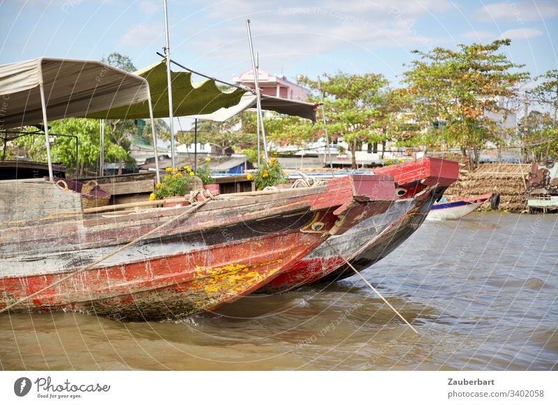 Zwei rote Boote vor grünem Hintergrund auf einem schwimmenden Markt im Mekong-Delta, Vietnam Wasser Wasserfahrzeug Farbfoto Außenaufnahme Asien Ruhe Eleganz