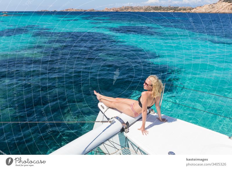 Frau entspannt sich auf einem Sommer-Segeltörn auf einem Luxus-Katamaran in der Nähe des bildschönen weißen Sandstrandes auf der Insel Spargi im Maddalena-Archipel, Sardinien, Italien.