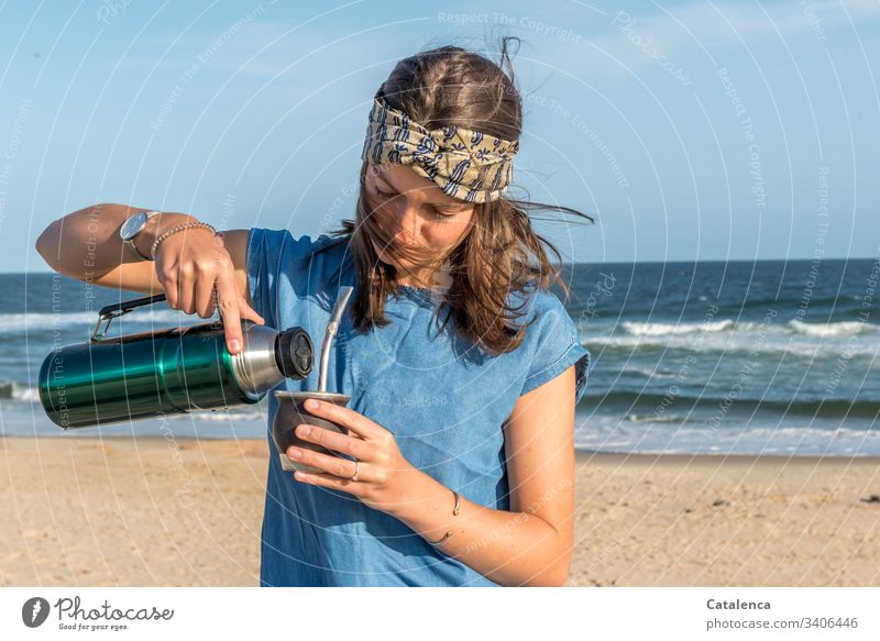 Junge Frau am Strand mit Matetee Person weiblich Sand Wellen Wasser Meer Thermoskanne windig Stirnband Sommer schönes Wetter Himmel Horizont Tag Tageslicht Blau