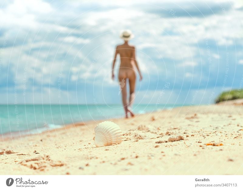 ein junges nacktes Mädchen mit Hut geht an einem leeren Strand in der Nähe der Meeresbrandung gegen den blauen Himmel mit Wolken im Sommer allein Unschärfe