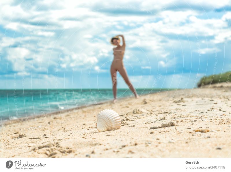 ein junges nacktes Mädchen mit Hut geht an einem leeren Strand in der Nähe der Meeresbrandung gegen den blauen Himmel mit Wolken im Sommer allein Unschärfe