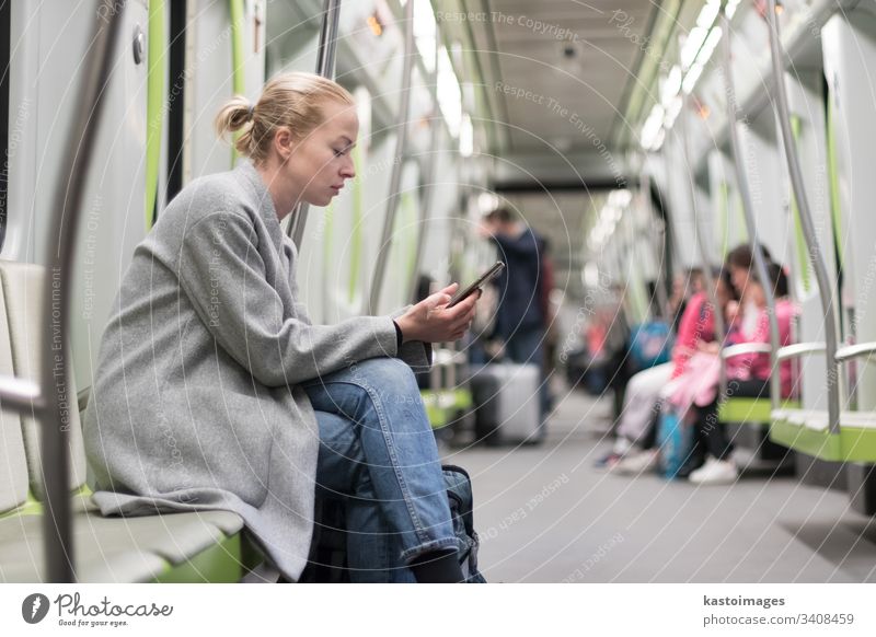 Hübsche blonde Frau im Wintermantel, die während der Fahrt mit den öffentlichen Verkehrsmitteln der U-Bahn am Telefon liest. Großstadt Passagier urban Zug