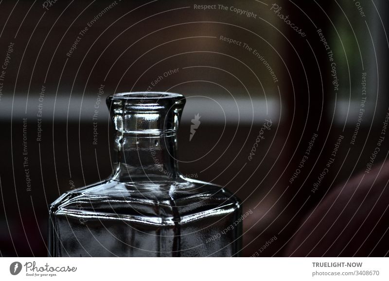 Morgenlicht fängt sich leuchtend in einer kantigen Flasche aus dickem Glas, während unscharf im Hintergrund ein heller Fensterrahmen die Düsternis unterbricht.