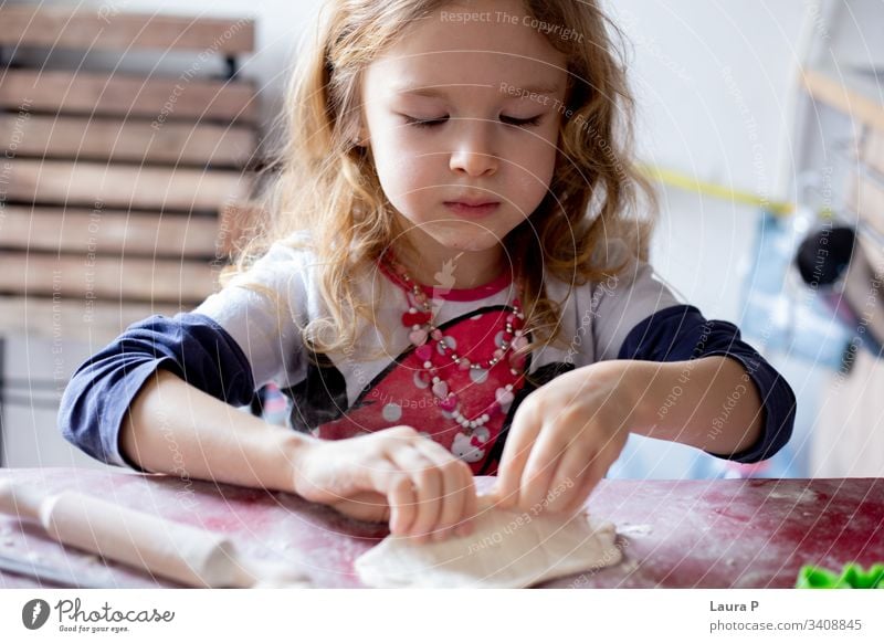 Hübsches blondes kleines Mädchen spielt mit Teig wenig schön lockig Behaarung Essen zubereiten backen Teigwaren Tisch doughtnuts Backwaren Farbfoto Mehl