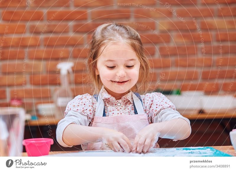 Kleines Mädchen isst den Puderzucker, der nach dem Backen von Keksen übrig bleibt. Kind nimmt am Backworkshop teil. Backkurse für Kinder, aufstrebende kleine Köche. Kochen lernen. Kombinieren und Rühren von vorbereiteten Zutaten. Echte Menschen, authentische Situationen