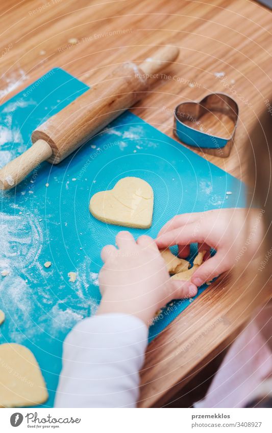 Kleines Mädchen schneidet den Teig für die Kekse in Herzform. Kind, das am Backworkshop teilnimmt. Backkurse für Kinder, aufstrebende kleine Köche. Mädchen, die kochen lernen. Kombinieren und Rühren von vorbereiteten Zutaten. Echte Menschen, authentische Situationen